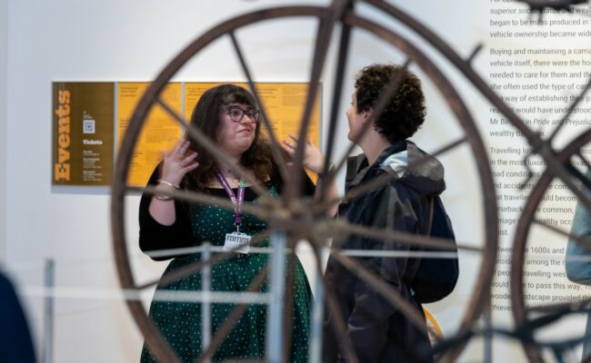 RAMM assistant curator speaks to a member of the public during a private view of a transport exhibition