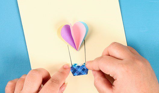 A pair of hands uses coloured card to create a two-dimensional hot air balloon