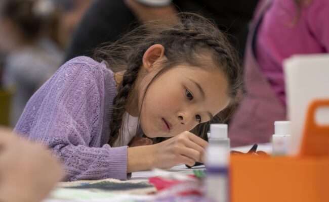 A young girl wearing a purple top takes part in a craft activity